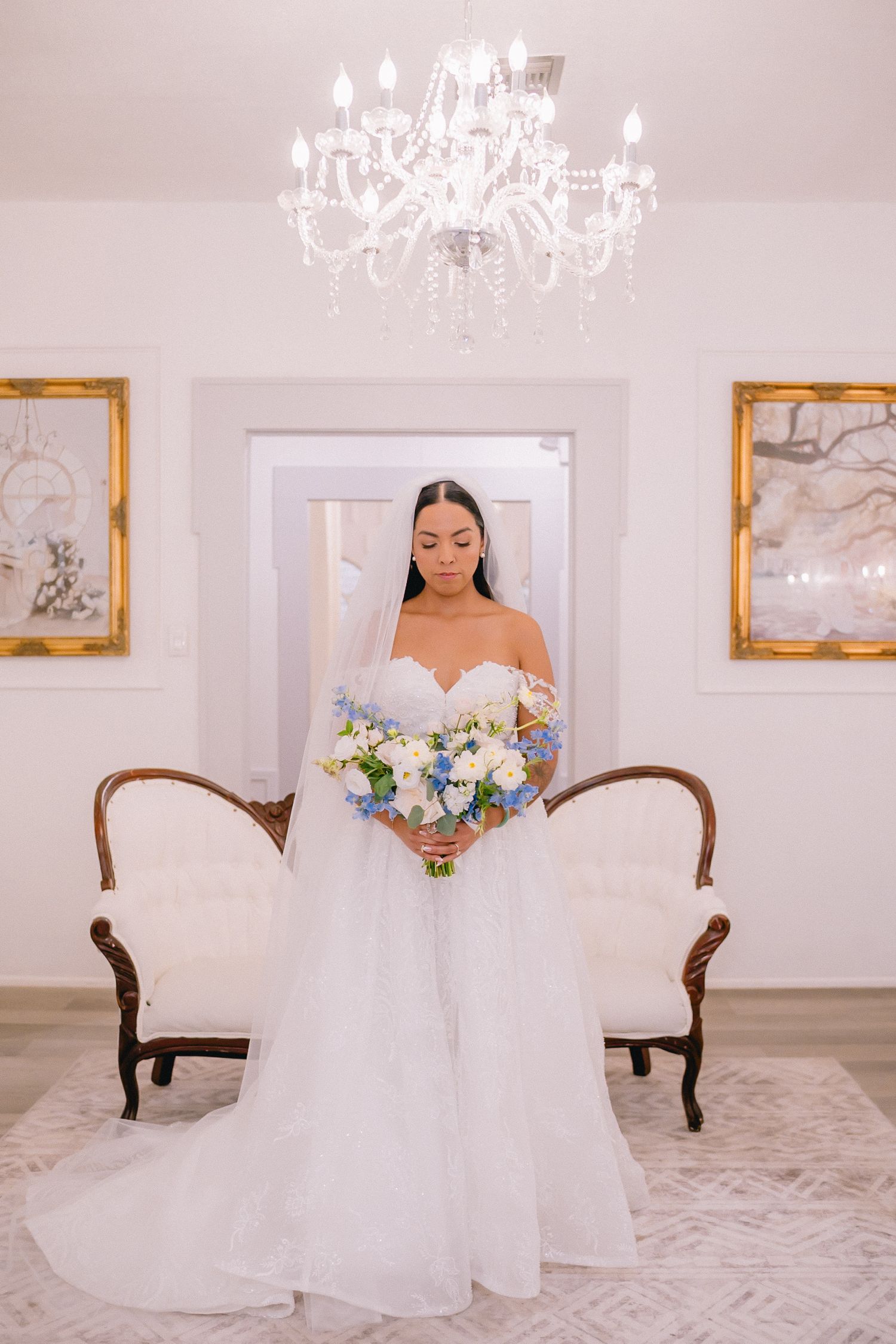 Elegant bridal portraits in white ballgown under crystal chandeliers in luxurious room.