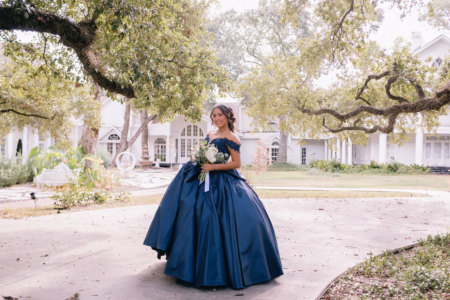 Majestic navy blue ball gown photographed under oak trees in a historic courtyard setting.