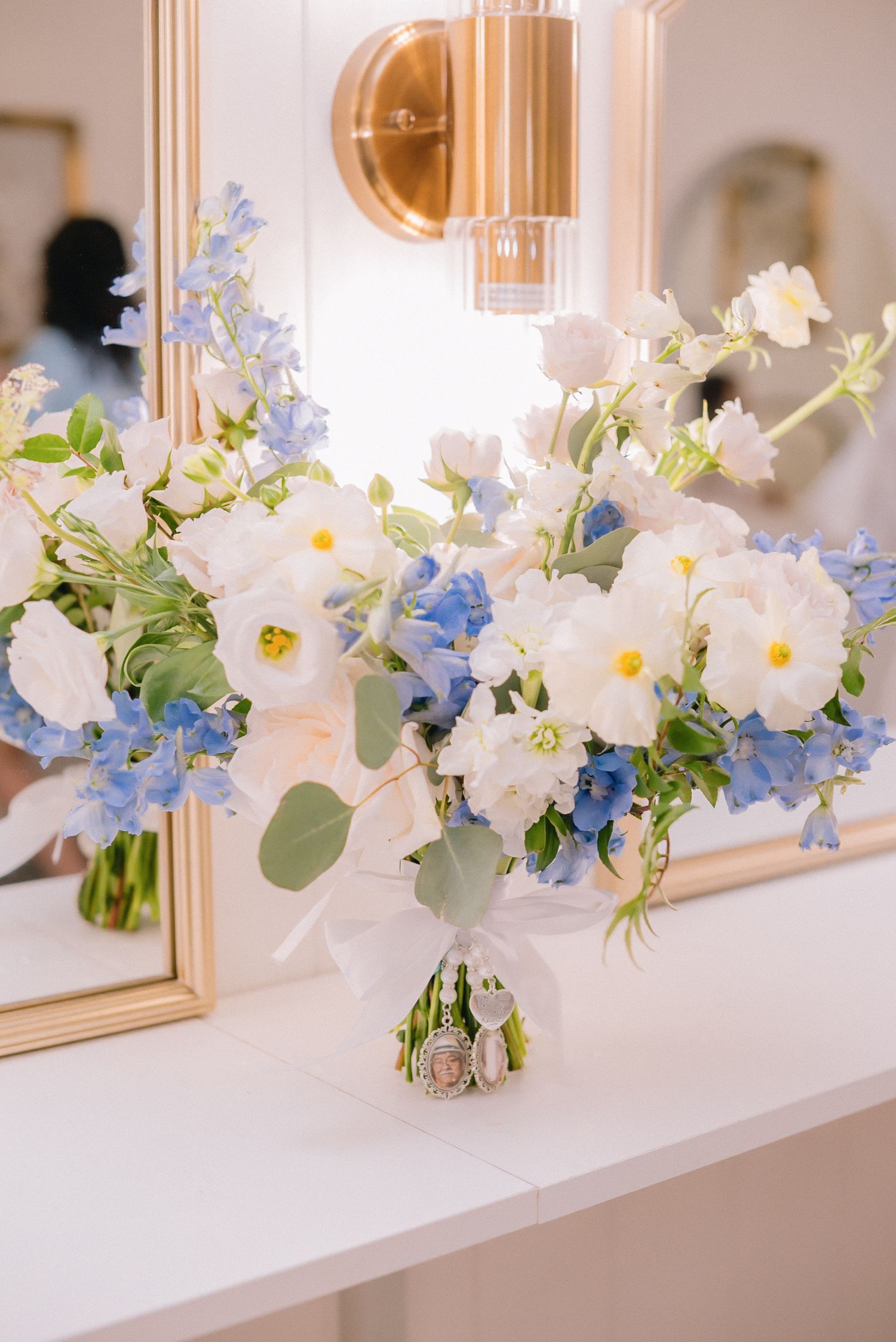 Delicate white and blue floral arrangements displayed on a white mantle with ornate mirrors.