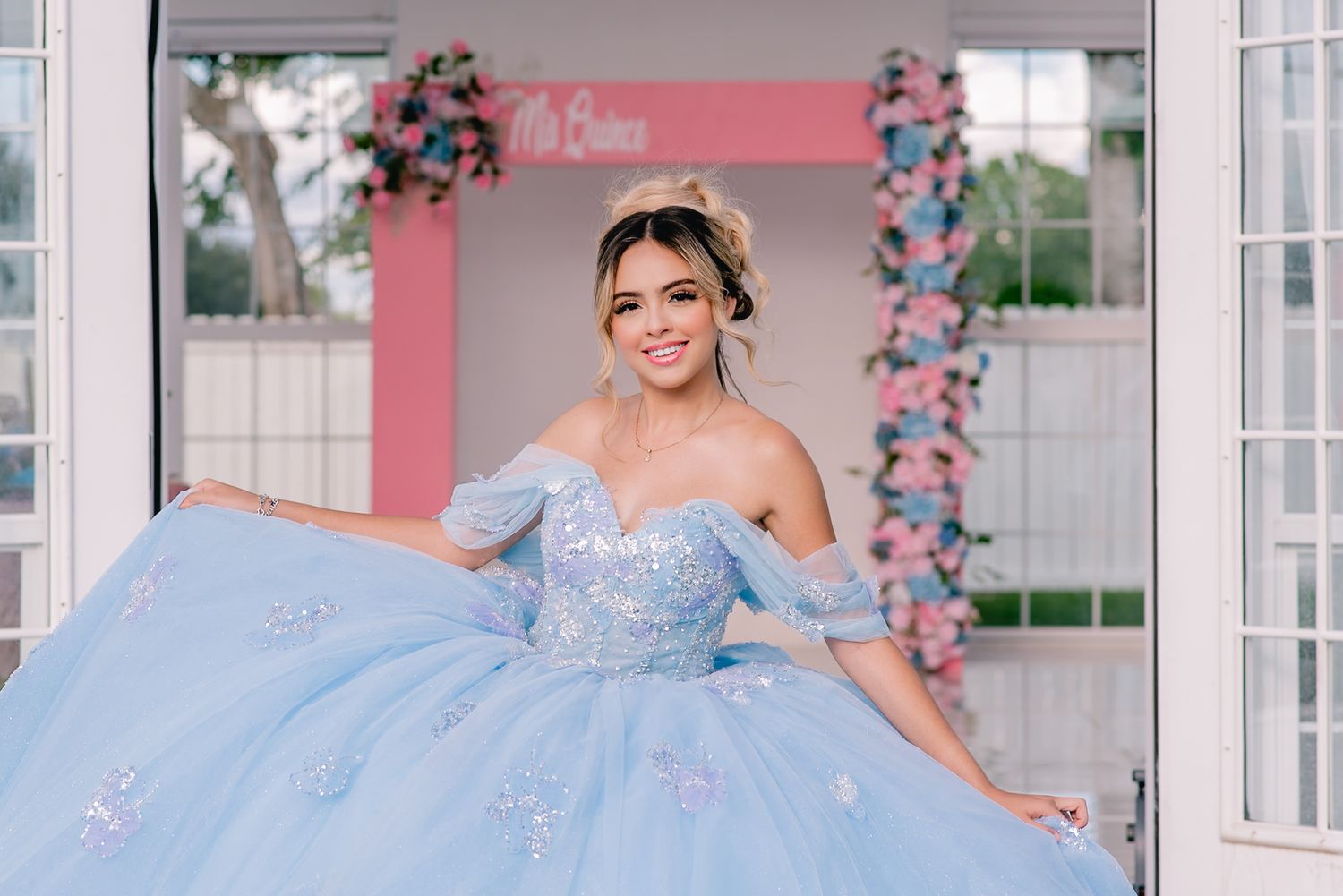 A glamorous powder blue ball gown captured in a bright venue with pink floral decorations.