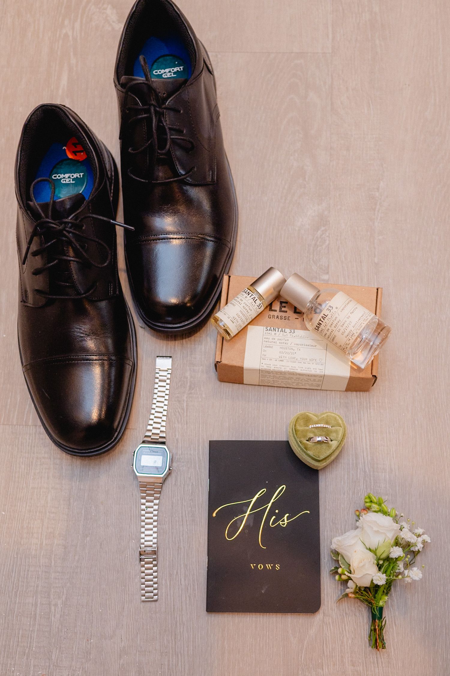 Wedding details flat lay with black dress shoes, boutonniere, and His card on beige background.