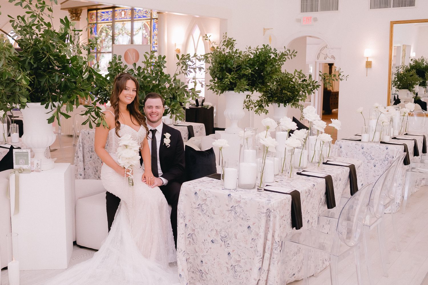 Modern white wedding reception hall decorated with black accents and hanging greenery.