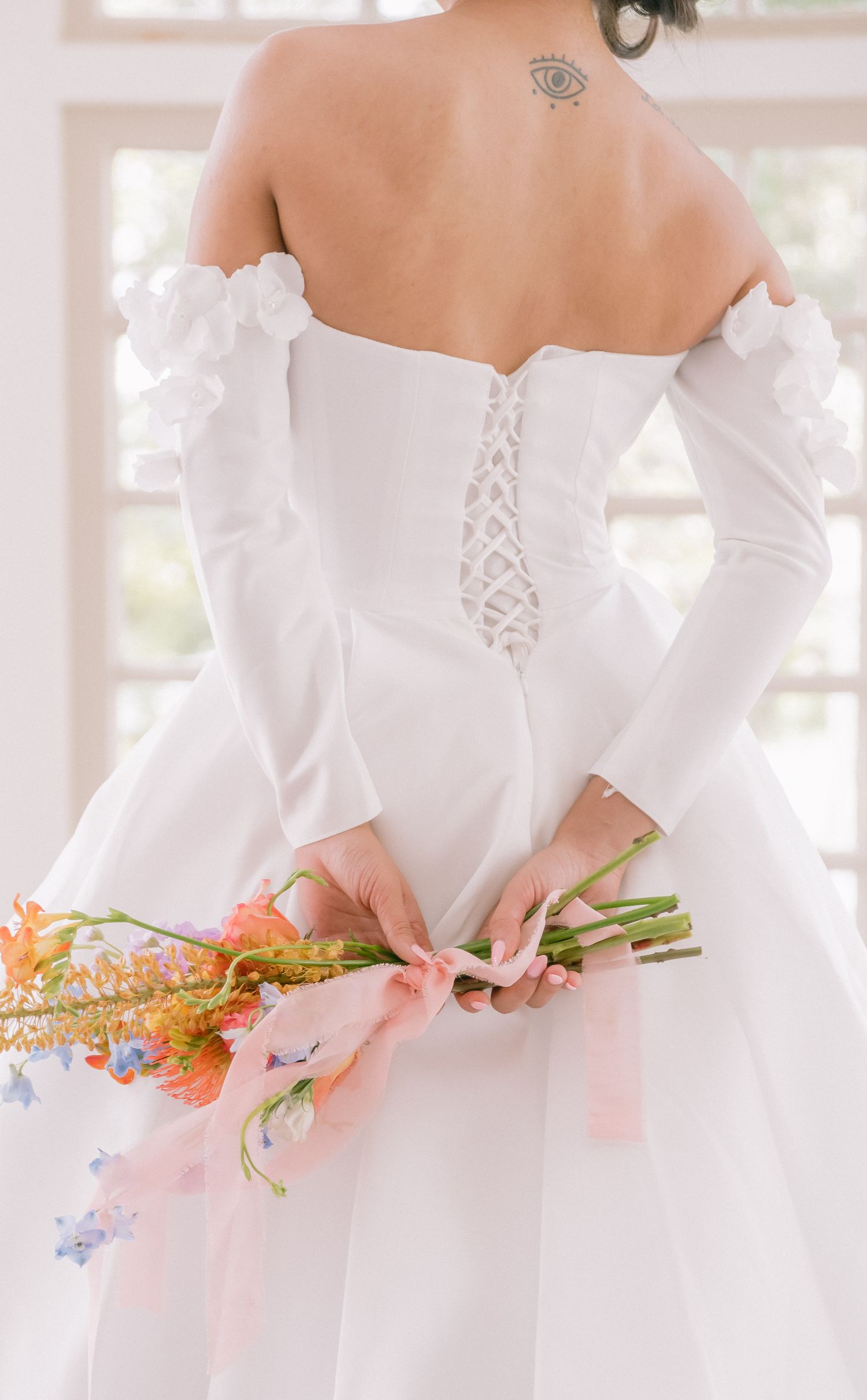 Back view of white wedding dress with corset lacing and off-shoulder sleeves.