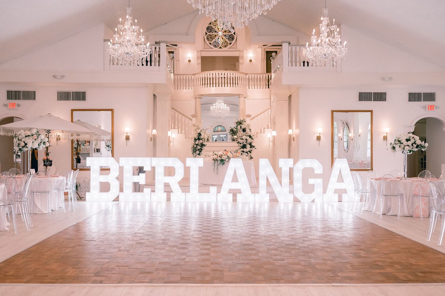 Elegant white ballroom with crystal chandeliers and large illuminated letters spelling BERLANGA.