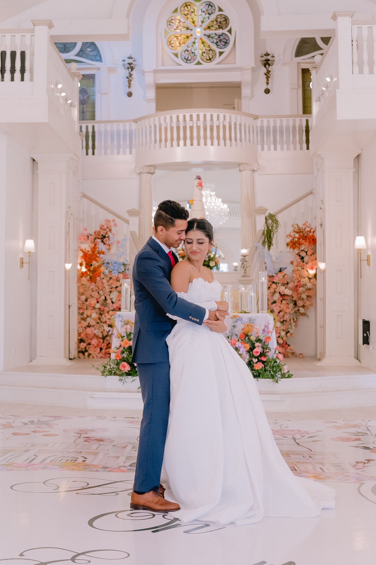 Wedding couple sharing an intimate moment in an elegant white ballroom with floral decor.