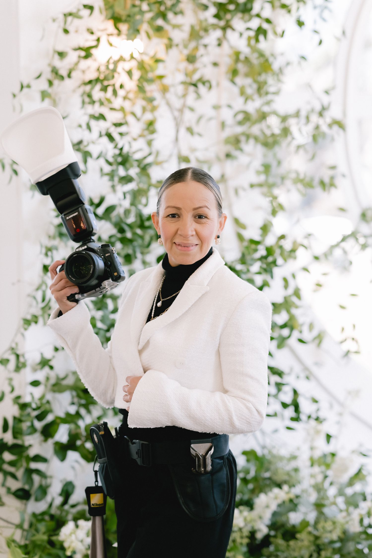 Professional photographer in white blazer and black pants holding camera equipment.