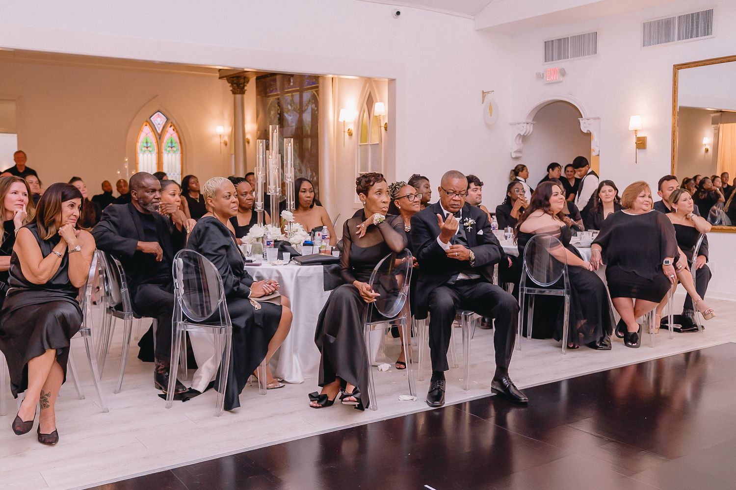 Wedding guests seated in rows at an elegant indoor reception venue with warm lighting.