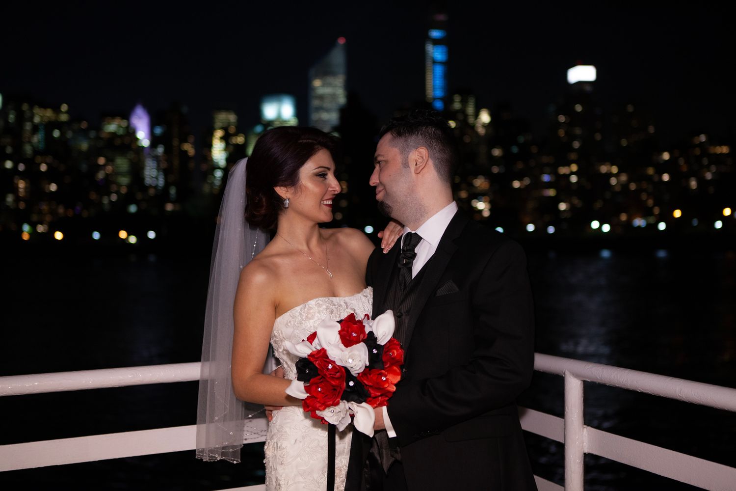 Romantic nighttime portrait of couple on waterfront terrace with city lights behind.