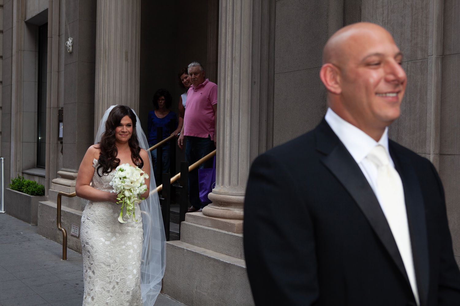 Formal wedding party members gathered outside a building with classical architecture.