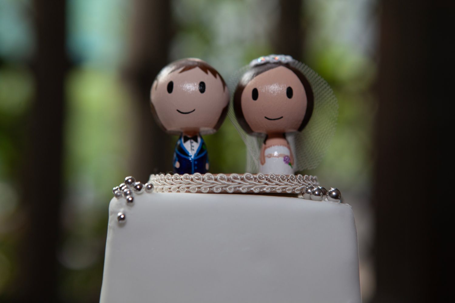 Cute wedding cake topper featuring cartoon-style bride and groom figurines smiling on a white frosted cake.