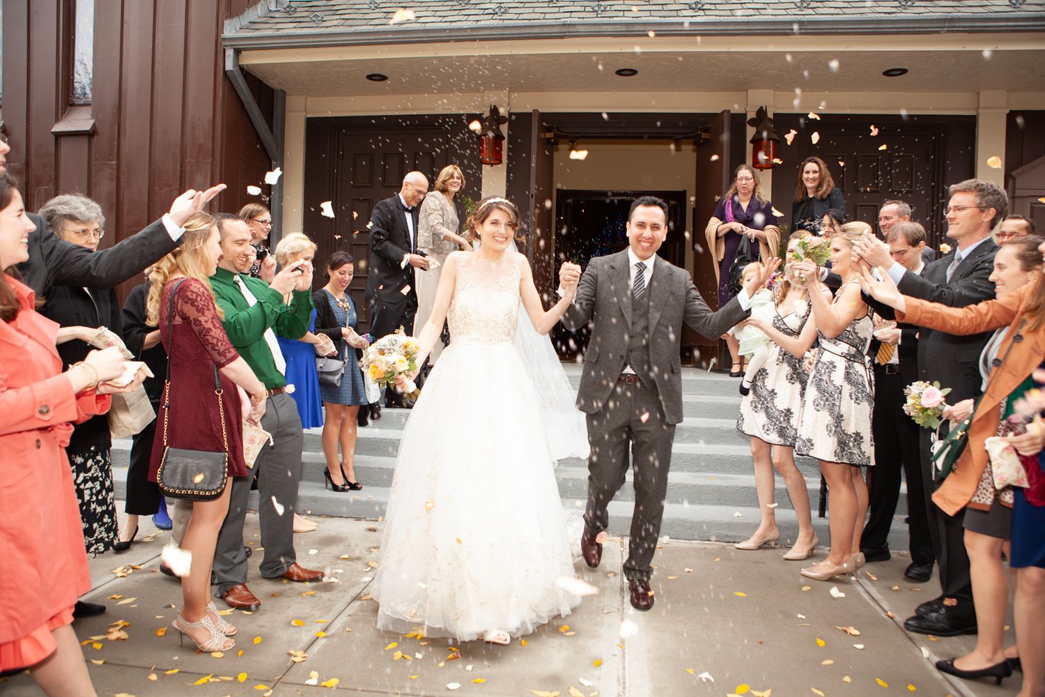 Happy newlyweds exit church while guests throw confetti in celebration.
