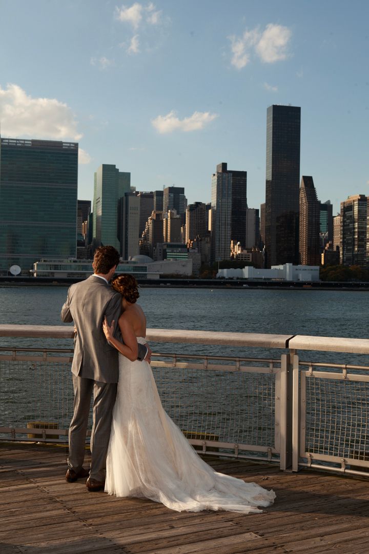 Couple in wedding attire viewing the Manhattan skyline from a wooden pier.