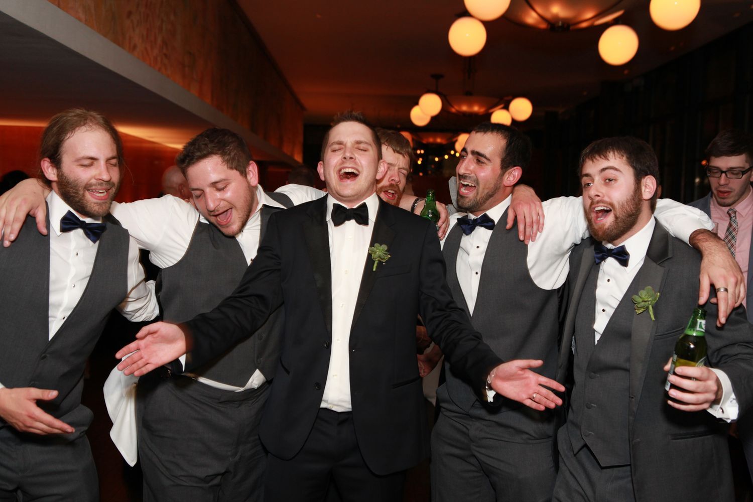 A group of groomsmen in formal attire celebrating joyfully at a wedding reception.