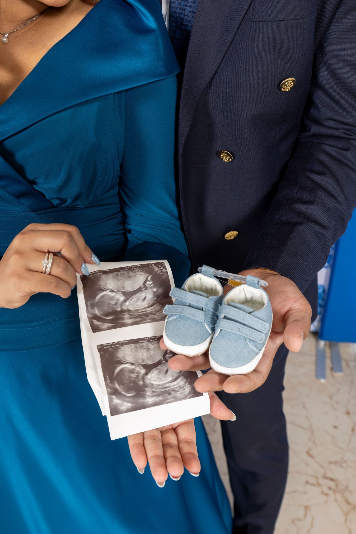 Couple holding ultrasound photo and tiny blue baby shoes in pregnancy announcement photo.