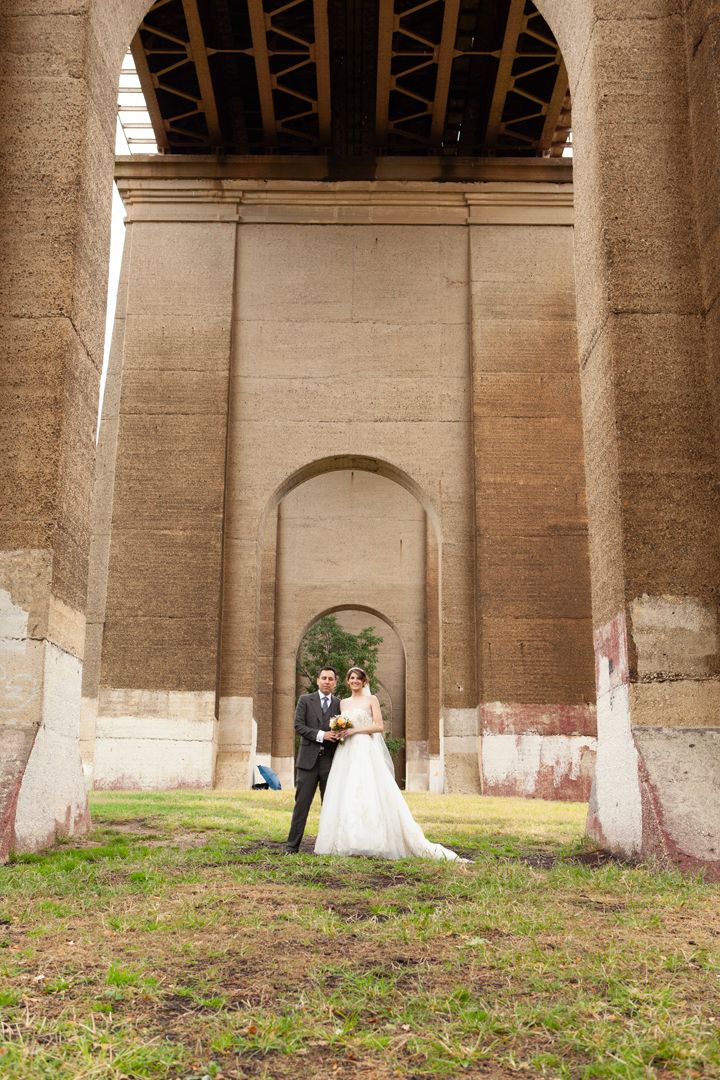 Wedding photo under a massive stone archway showing a couple in formal attire.