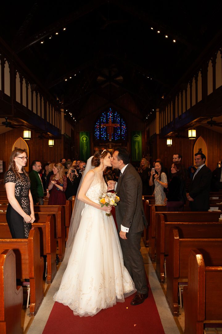 Romantic first kiss moment in church aisle with stained glass and wooden pews.