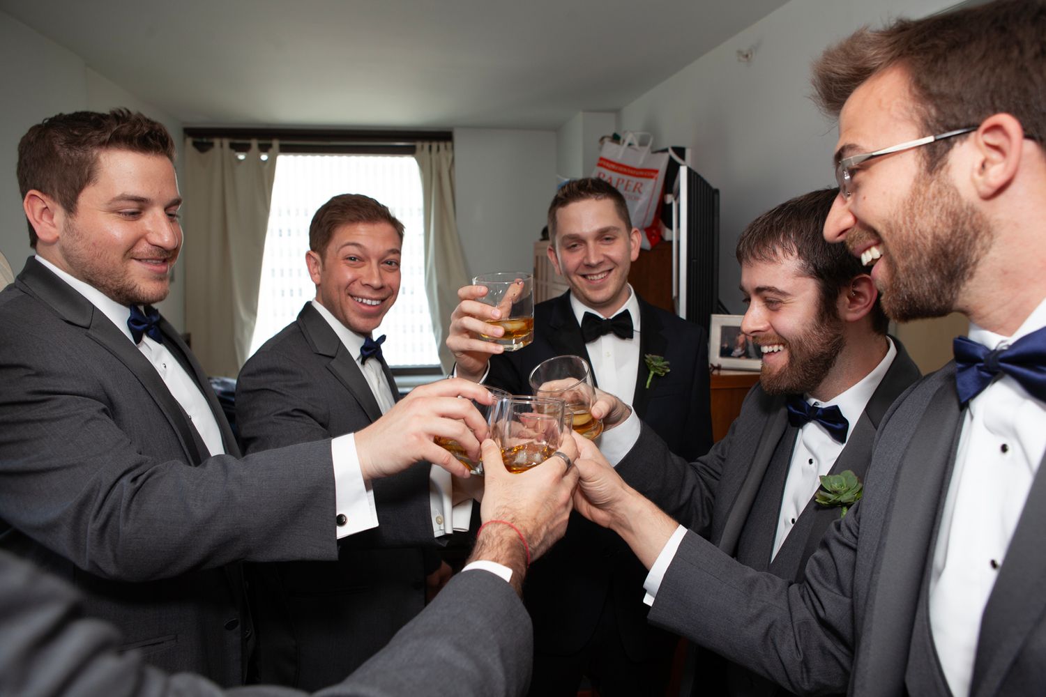 Groomsmen in tuxedos toast with drinks before the ceremony.