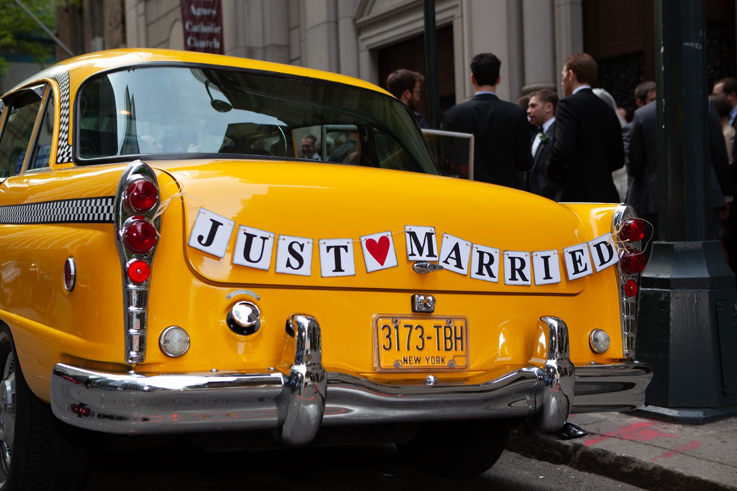 Yellow vintage taxi with 'Just Married' sign decorating the back bumper.
