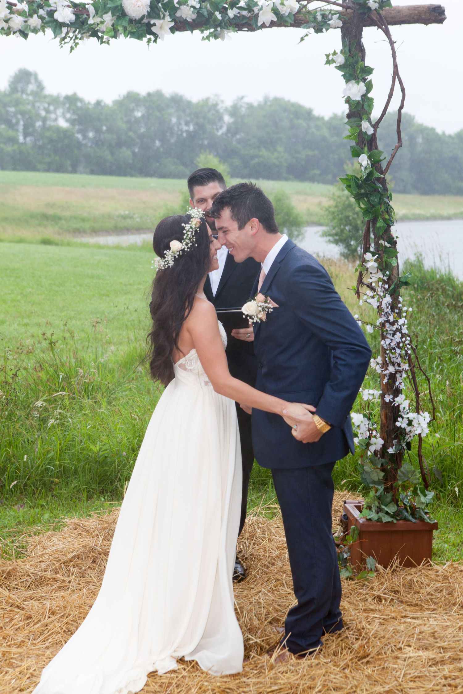 Newlyweds share their first kiss under a rustic floral arch during an outdoor countryside wedding ceremony.