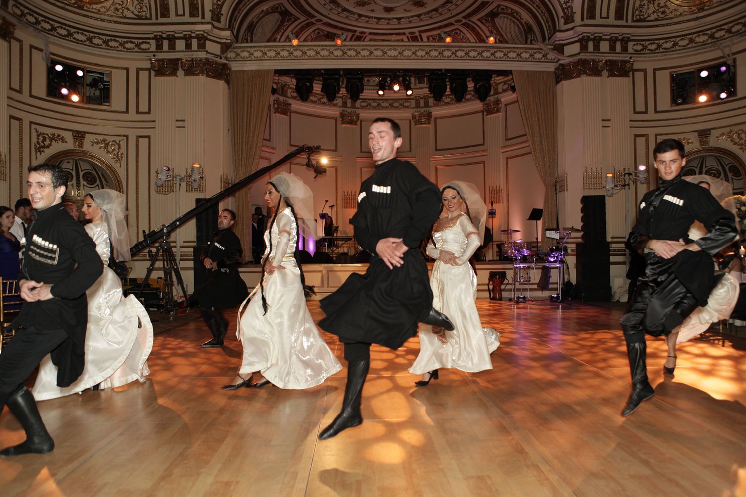 Dancers perform traditional folk dances in formal attire on a grand ballroom floor.