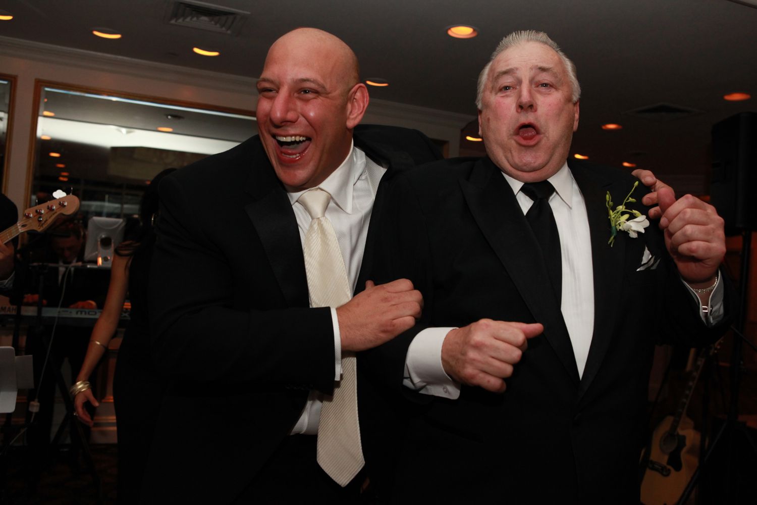 Two formally dressed people share a hearty laugh together at what appears to be a wedding reception or formal event.