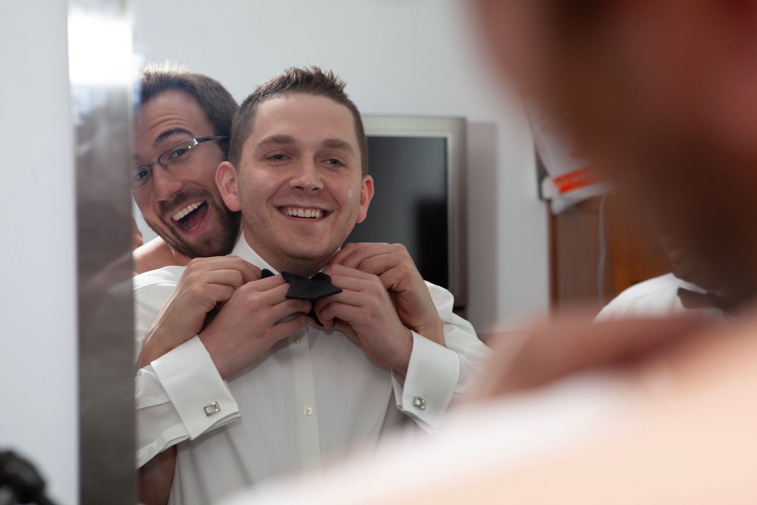 Two people adjusting a bowtie while getting ready in formal attire.