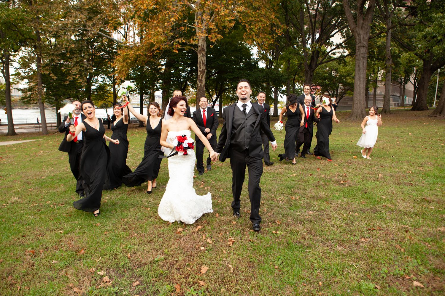 Wedding party walks across an autumn lawn with trees in the background.