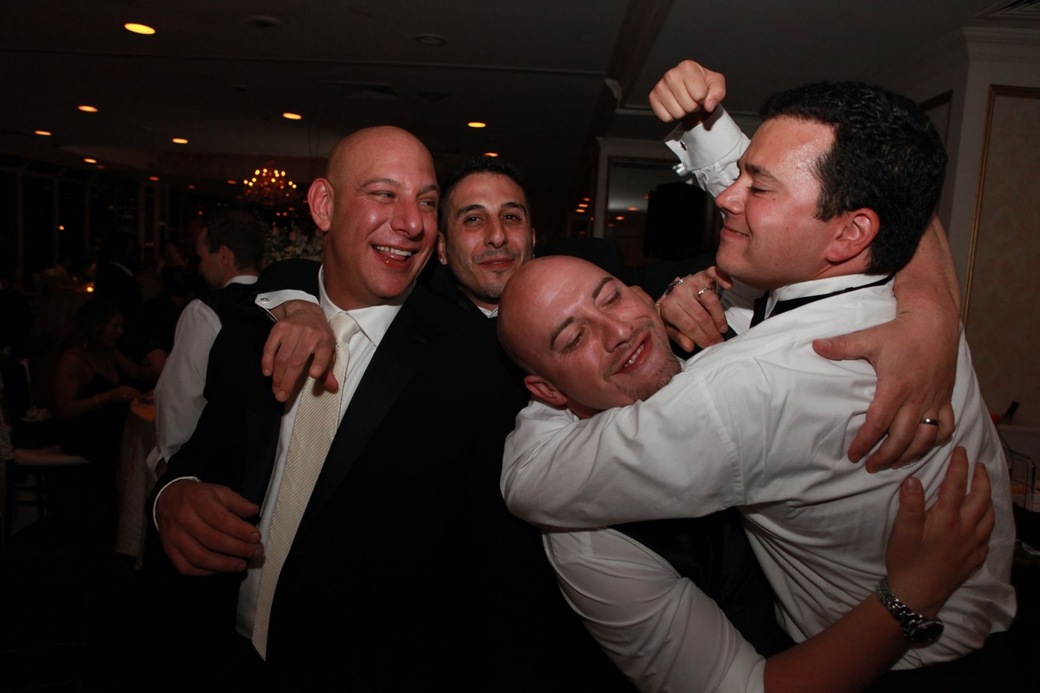 Wedding party members laughing and embracing during candid reception moments.