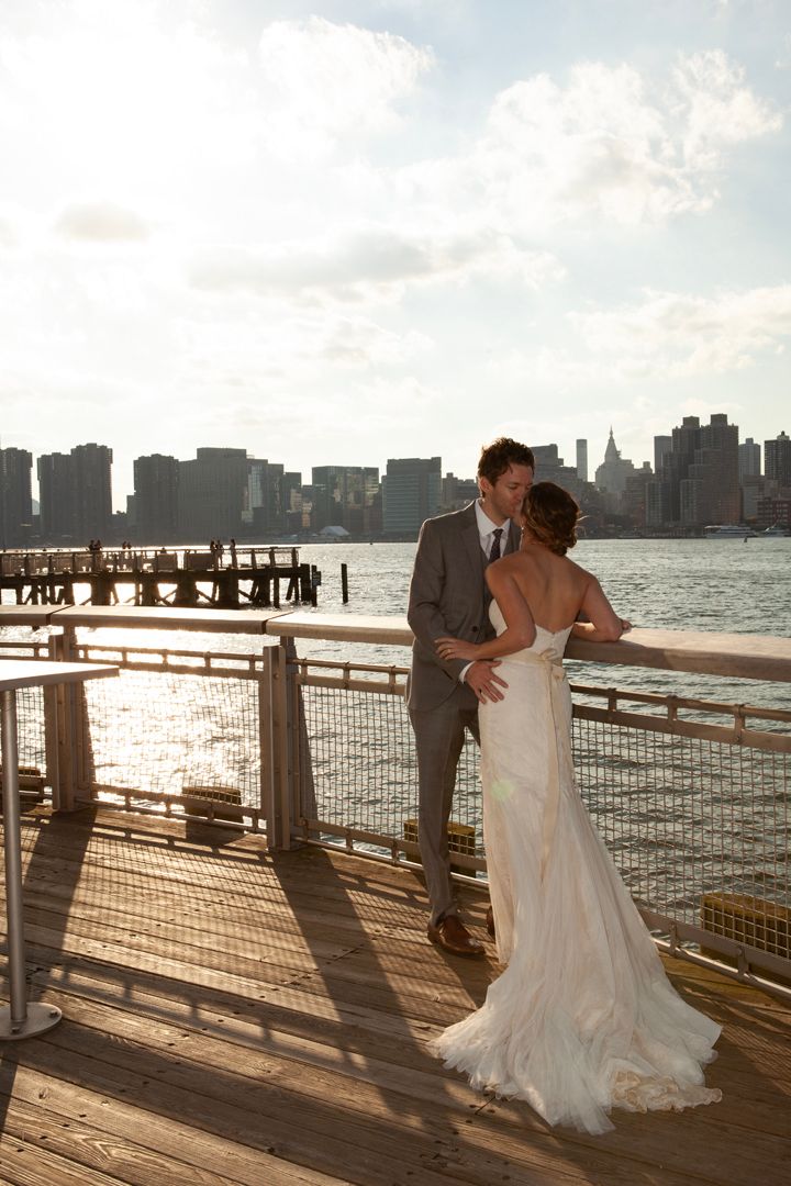 Wedding couple shares intimate moment on pier during golden hour with city skyline backdrop.