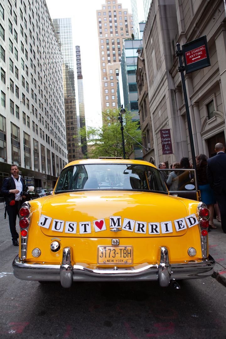 Rear view of yellow taxi with 'Just Married' sign between city buildings.