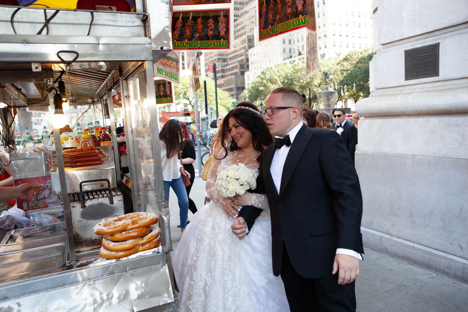 Wedding party posing near street vendors and food carts in an urban setting.