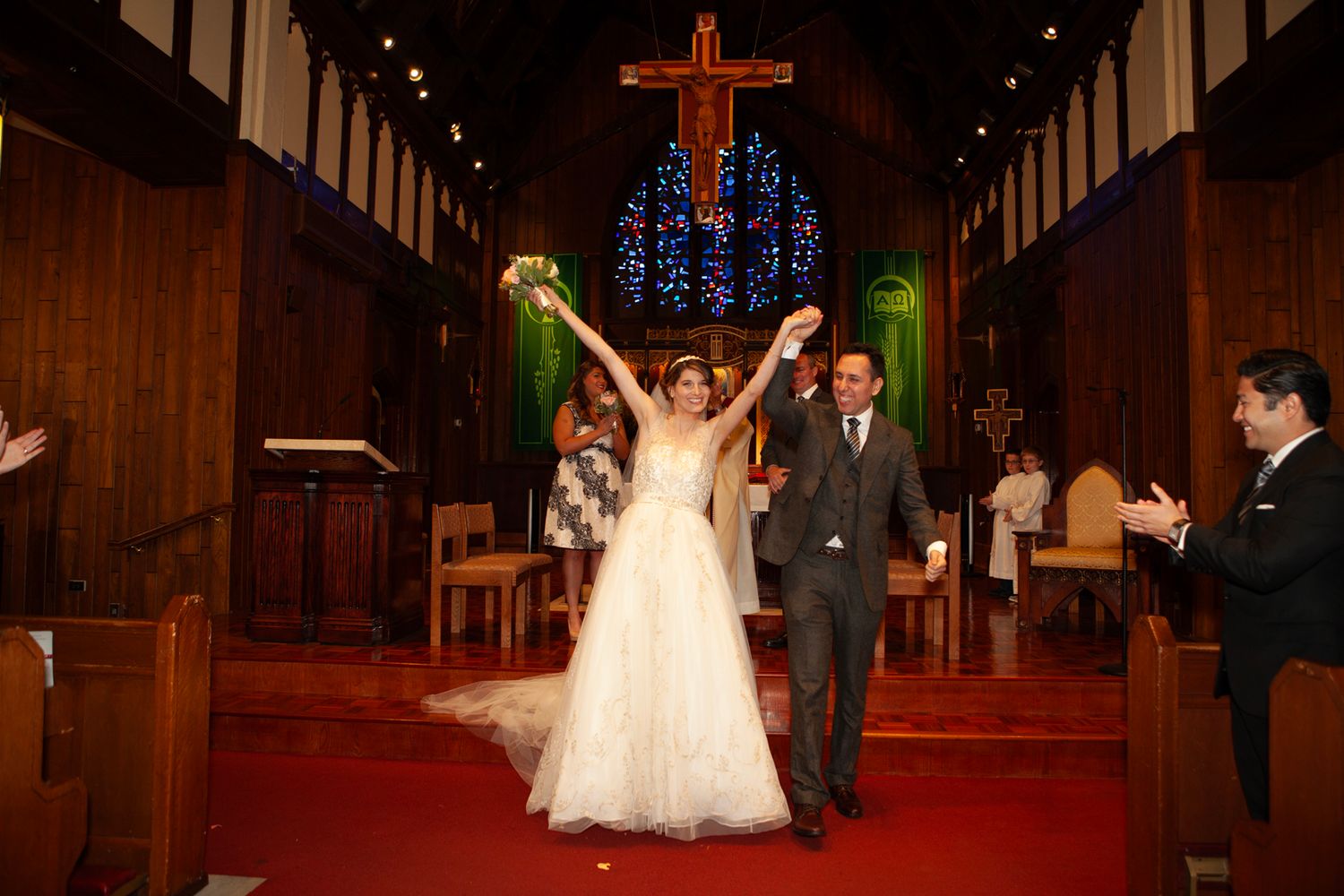 Joyful newlyweds celebrate at altar with raised arms under dramatic church lighting.