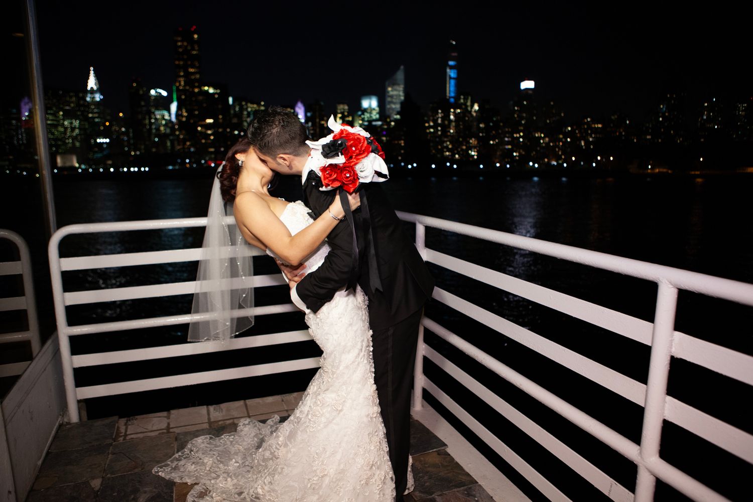 Intimate moment between couple on deck with illuminated cityscape in background.