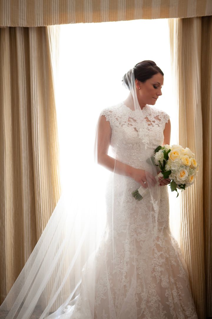 Bride in fitted lace wedding dress poses with yellow rose bouquet.