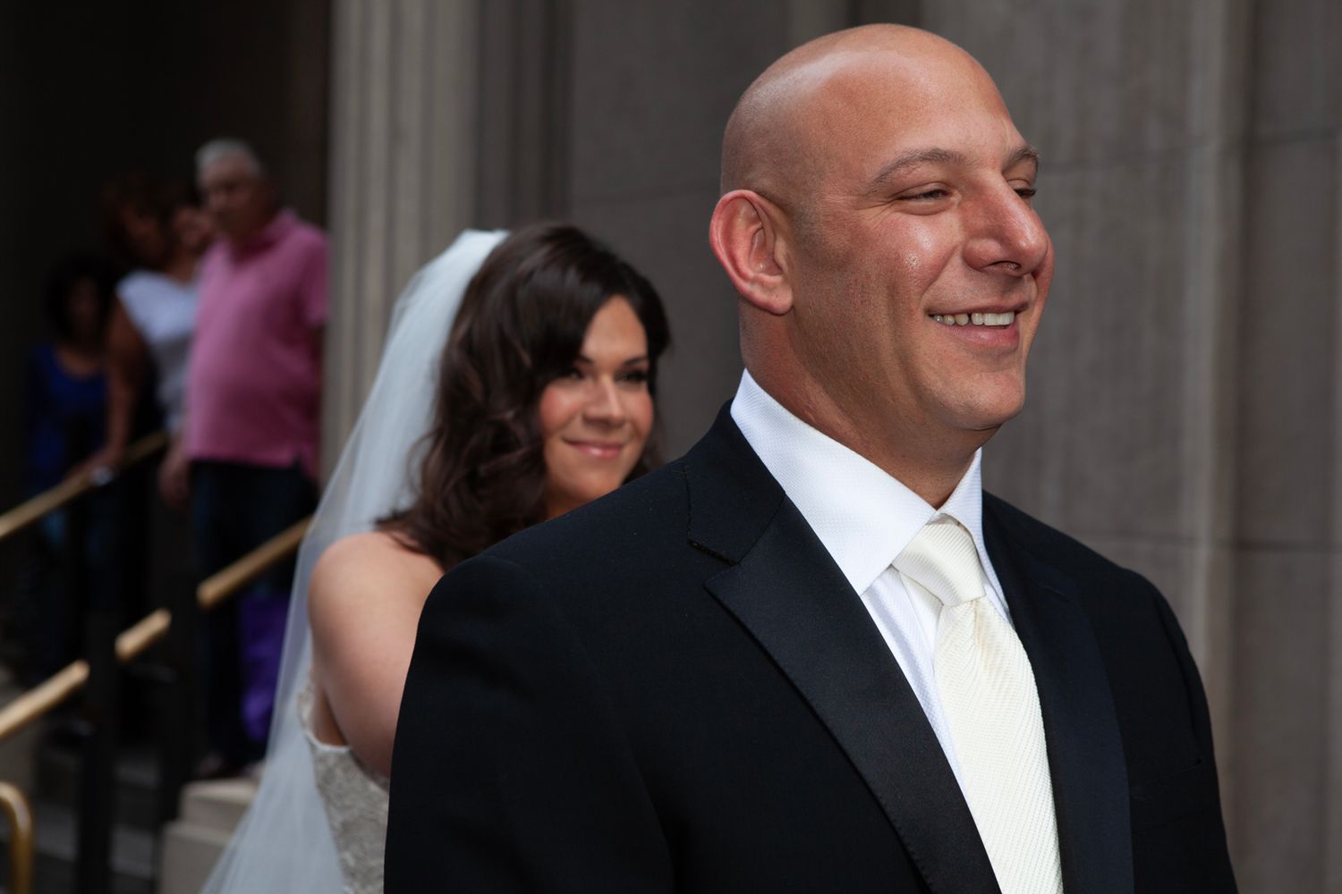 Wedding party members walk along exterior of building with classical columns.