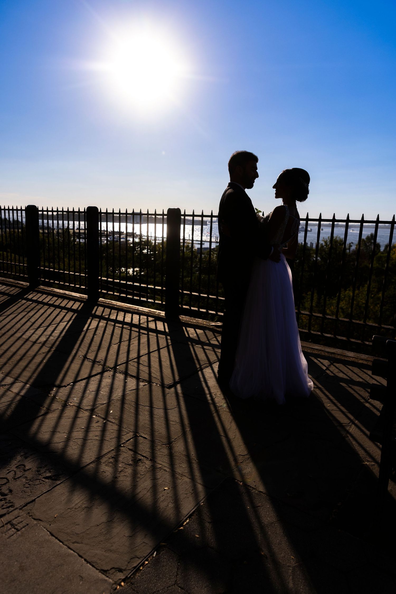 Two silhouettes cast dramatic shadows on a deck railing against a bright blue sky during sunset.