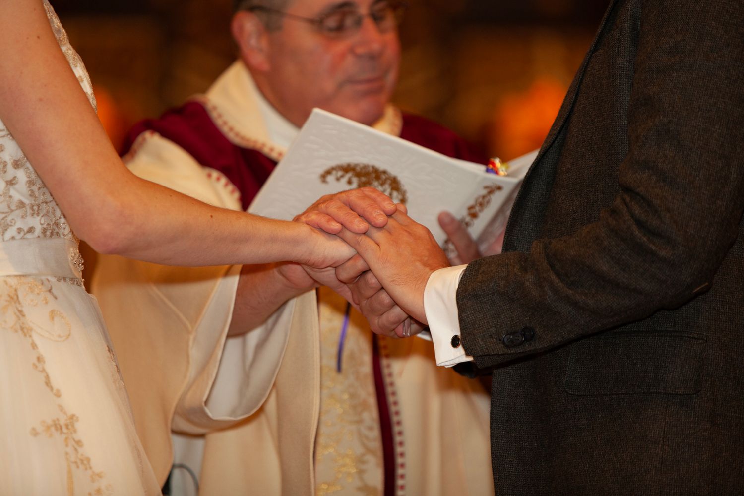 Close-up of hands exchanging rings during wedding ceremony with officiant in background.