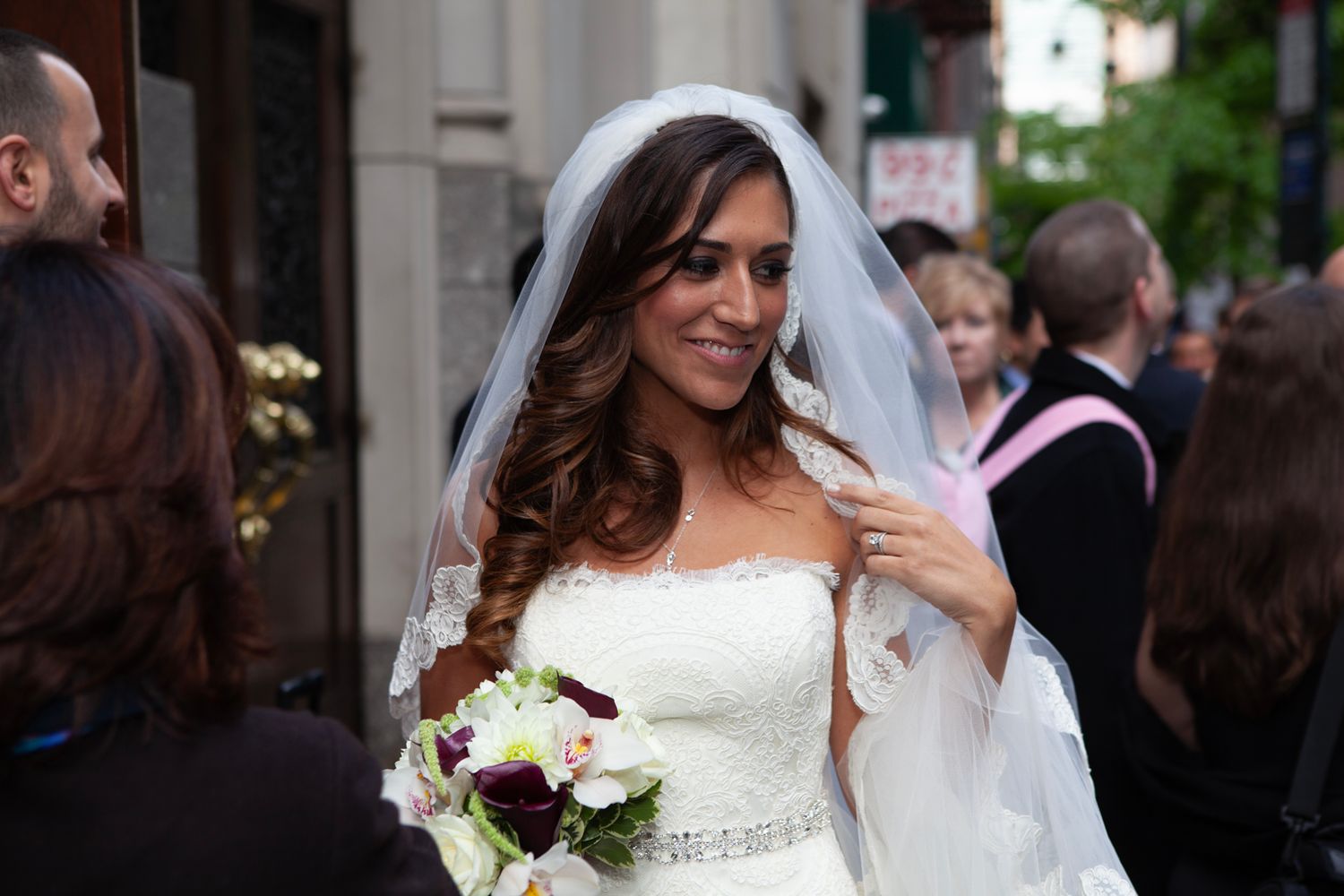 Bride in white dress holding red and white bouquet at outdoor ceremony.