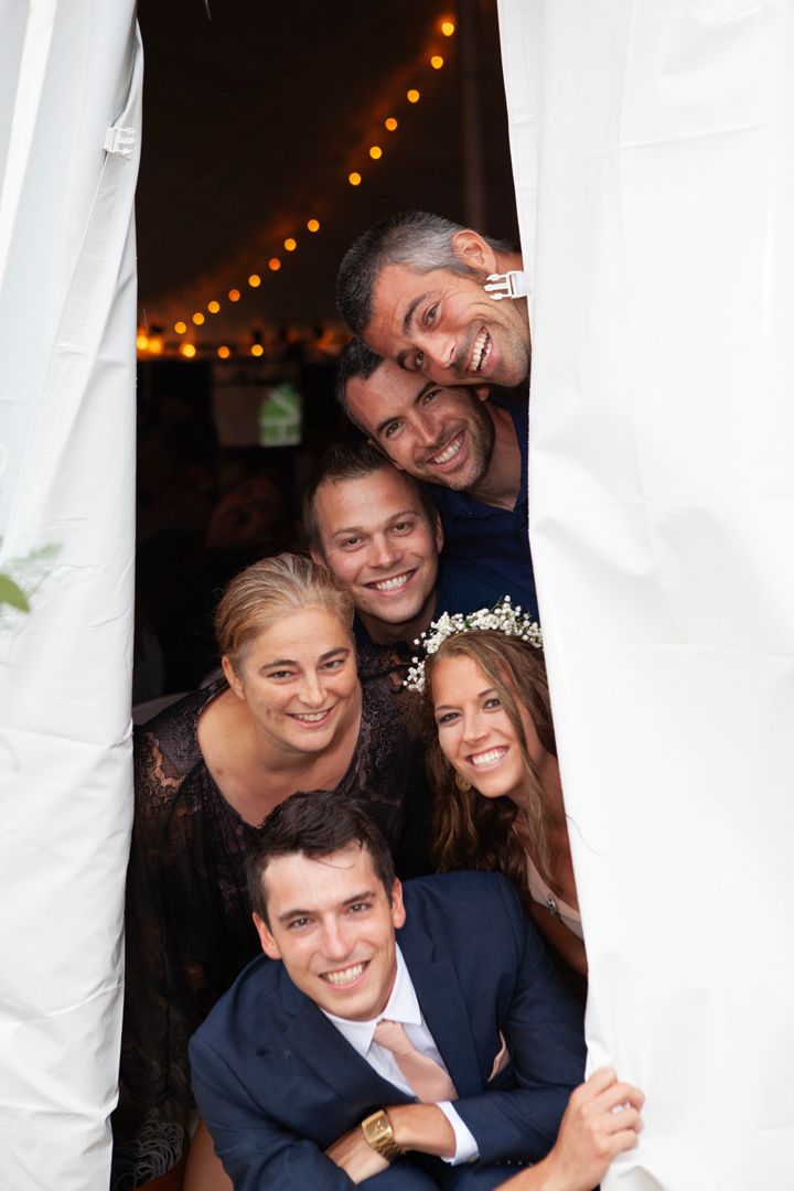 Group poses together through white tent opening with string lights visible above.