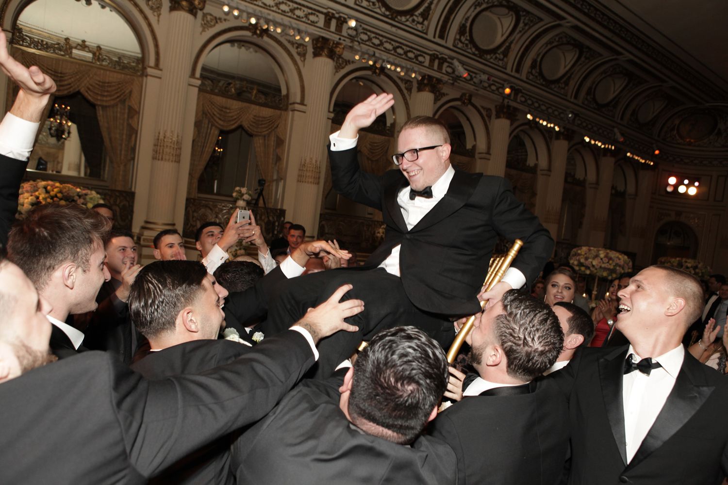 Groomsmen lift someone in celebration at an elegant formal event.