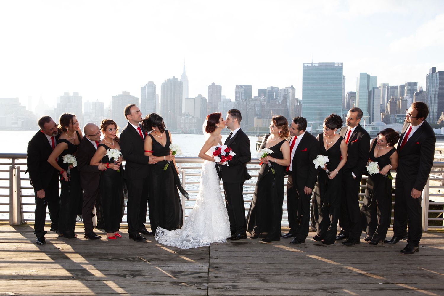 Wedding party poses for photos with New York City skyline in background.