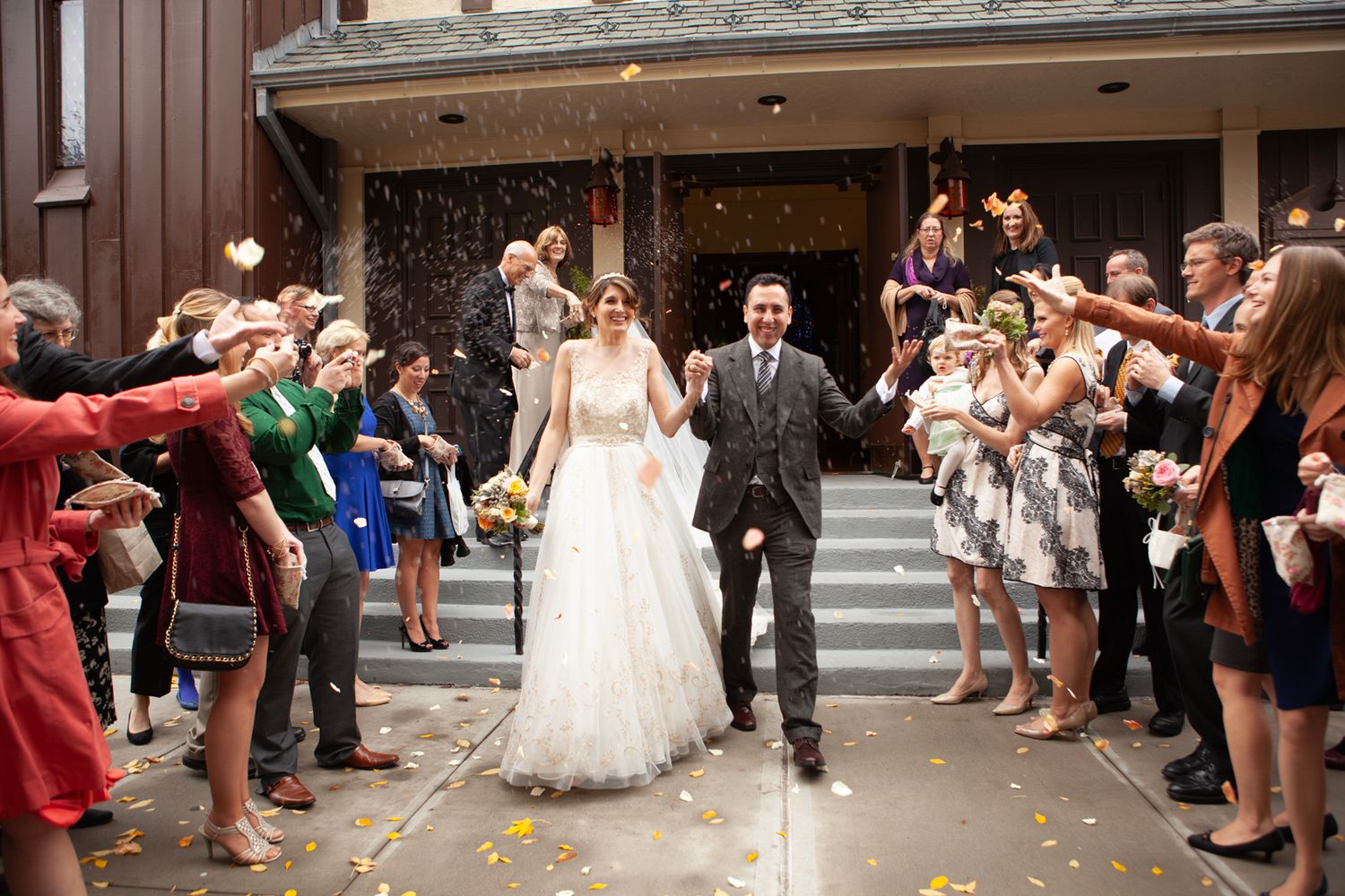 Bride and groom walk through crowd of cheering wedding guests throwing confetti.