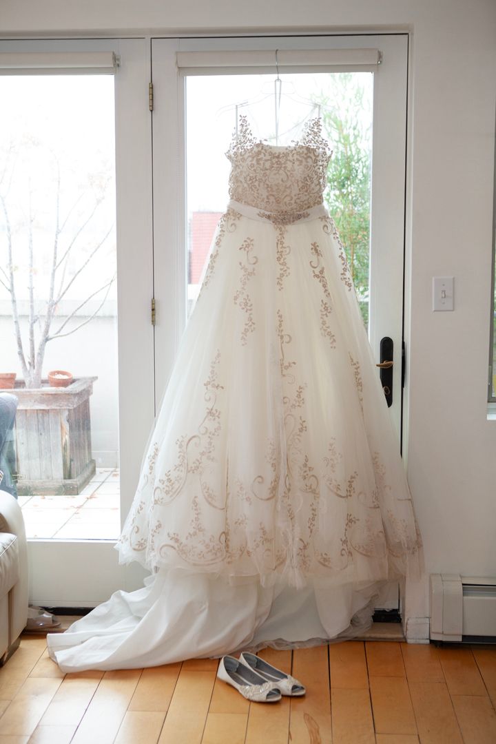 Beautiful wedding dress with intricate beading displayed in sunlit room with wooden floors.