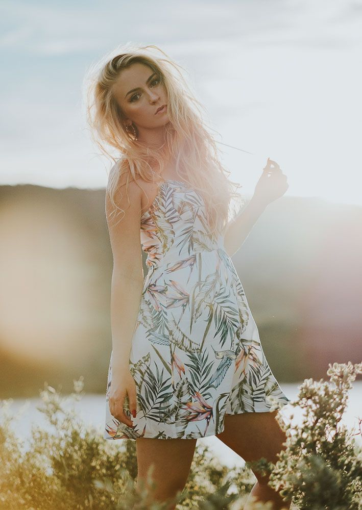 Woman in floral sundress posing in golden summer field at sunset.