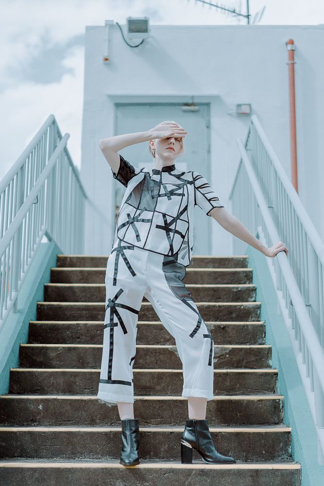 Person in modern black and white graphic outfit poses on light blue concrete stairs.