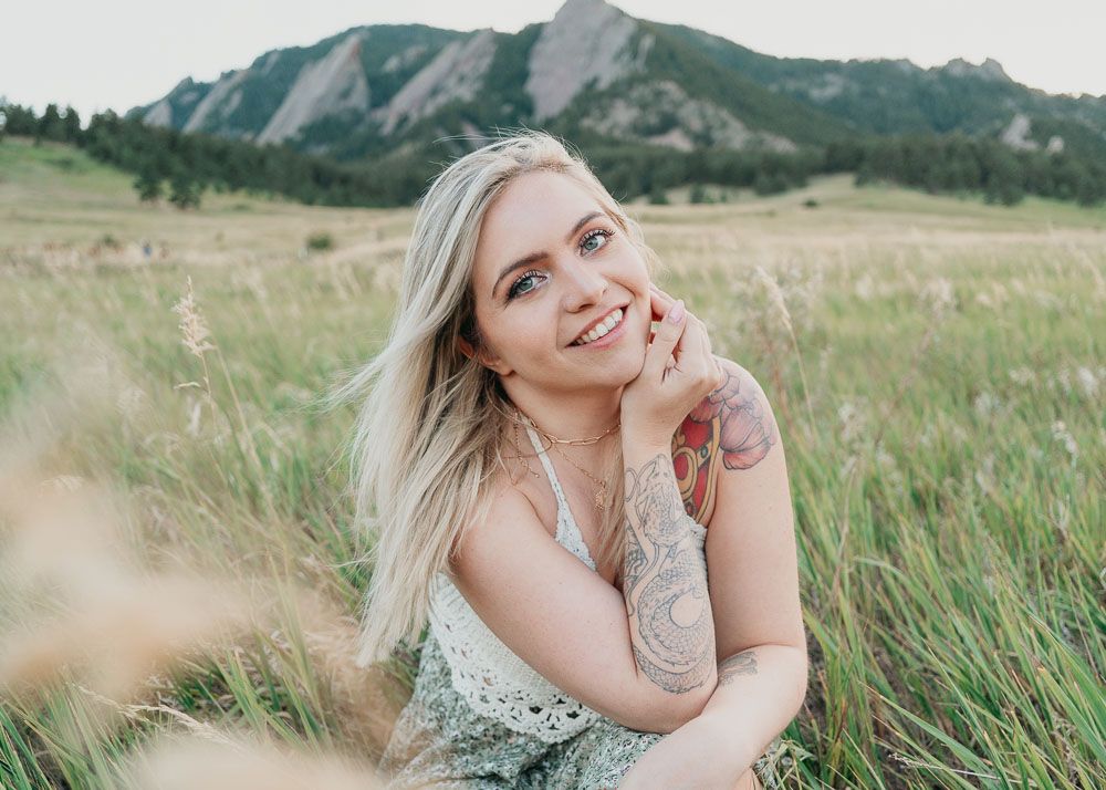 Portrait taken in a grassy field with mountain peaks in the background.