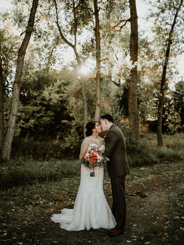 A romantic woodland wedding photo of a couple embracing at sunset among tall trees.