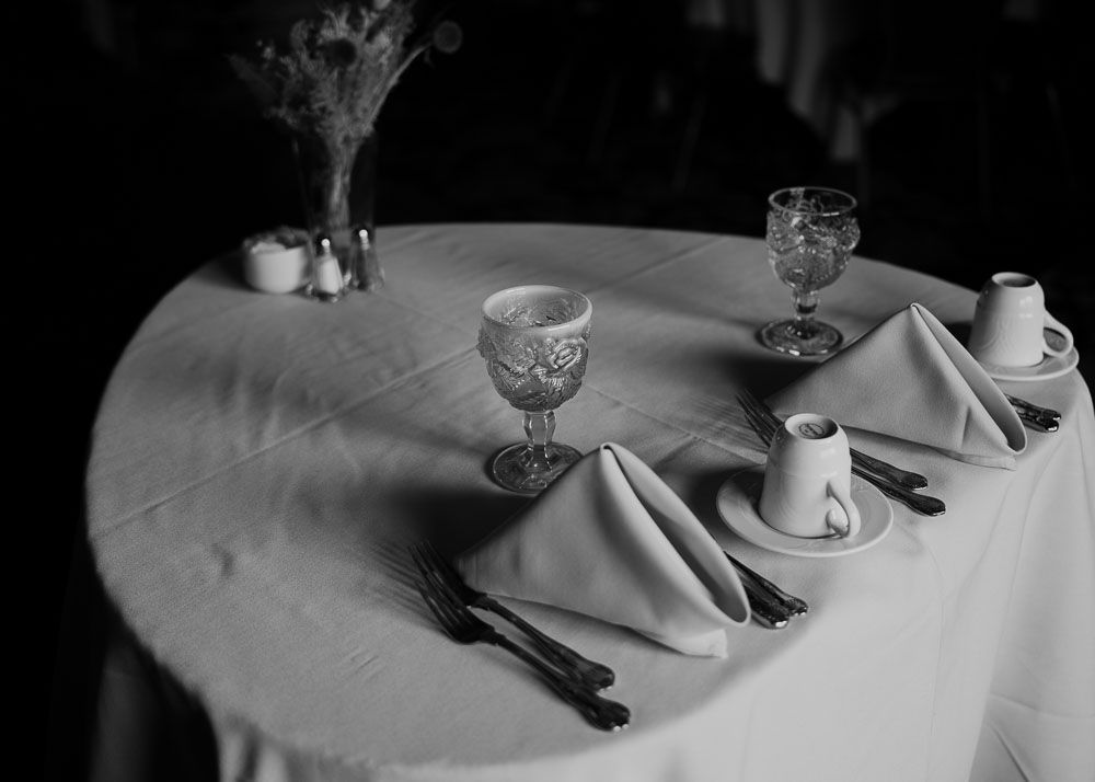 Formal place settings with wine glasses and folded napkins on round table with white tablecloth.