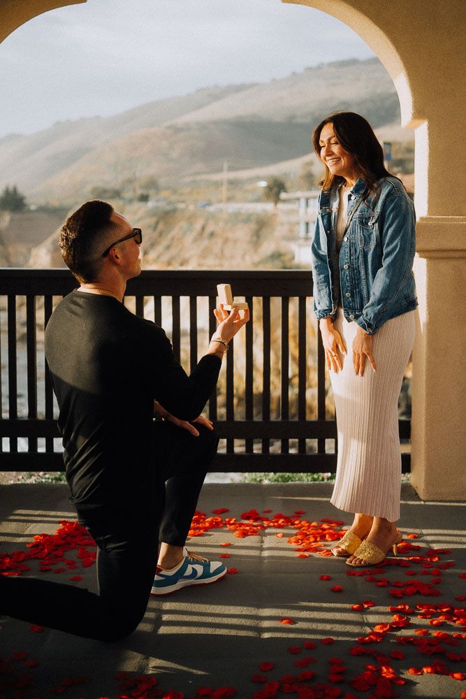 Marriage proposal sequence on a balcony decorated with rose petals overlooking mountains.