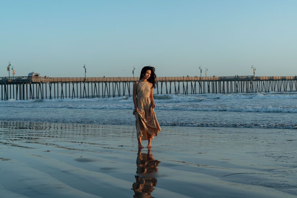 Ethereal beach portrait with long pier stretching into ocean at sunset.